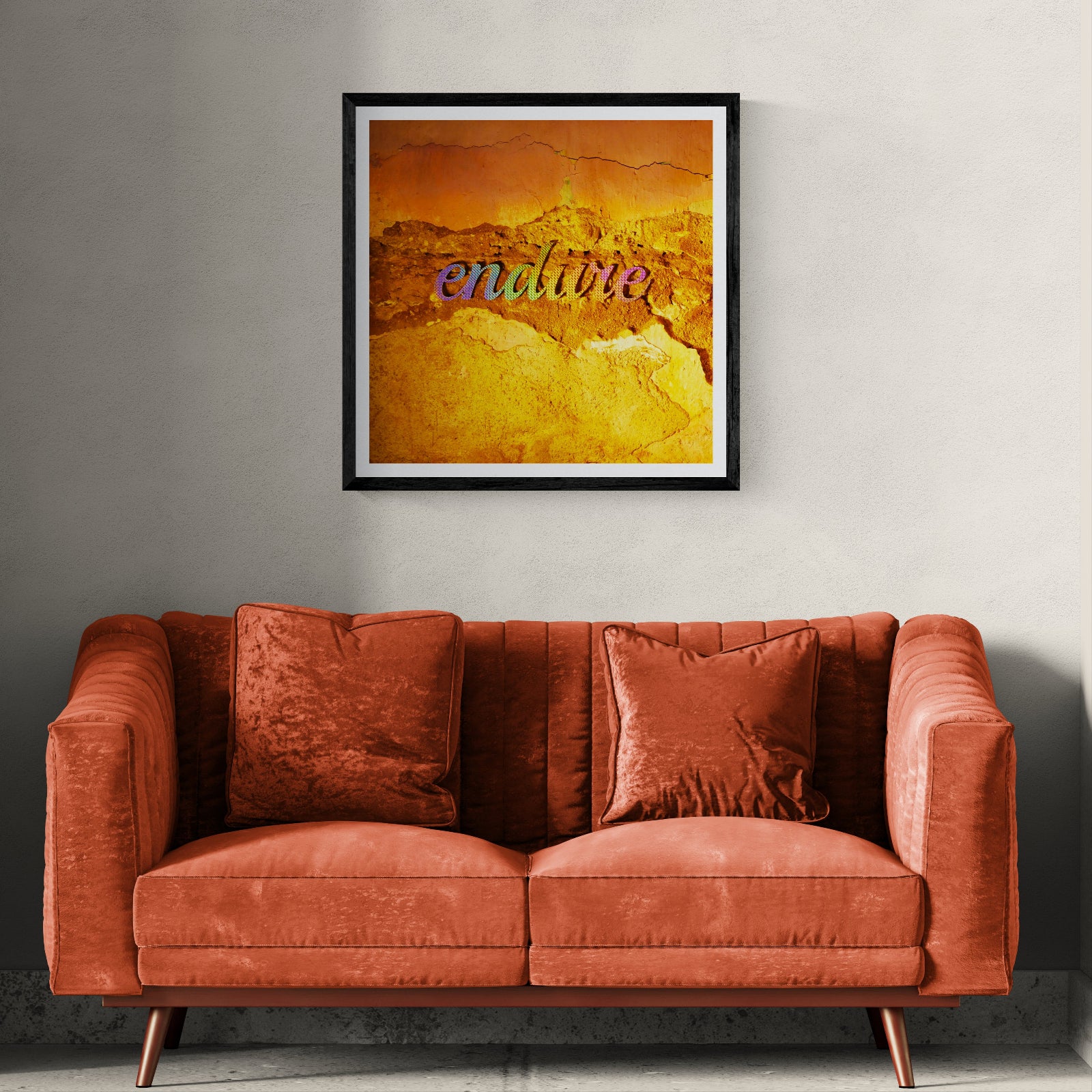 Endure iridescent typography art print on a weathered rust and ochre surface displayed as 30 × 30 wall art in a black frame above a burnt-orange sofa.