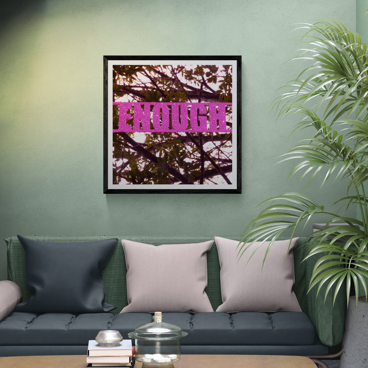 Enough pink glitter typography art print with botanical photography displayed as 30 × 30 wall art in a black frame above a green sofa in a modern living room.