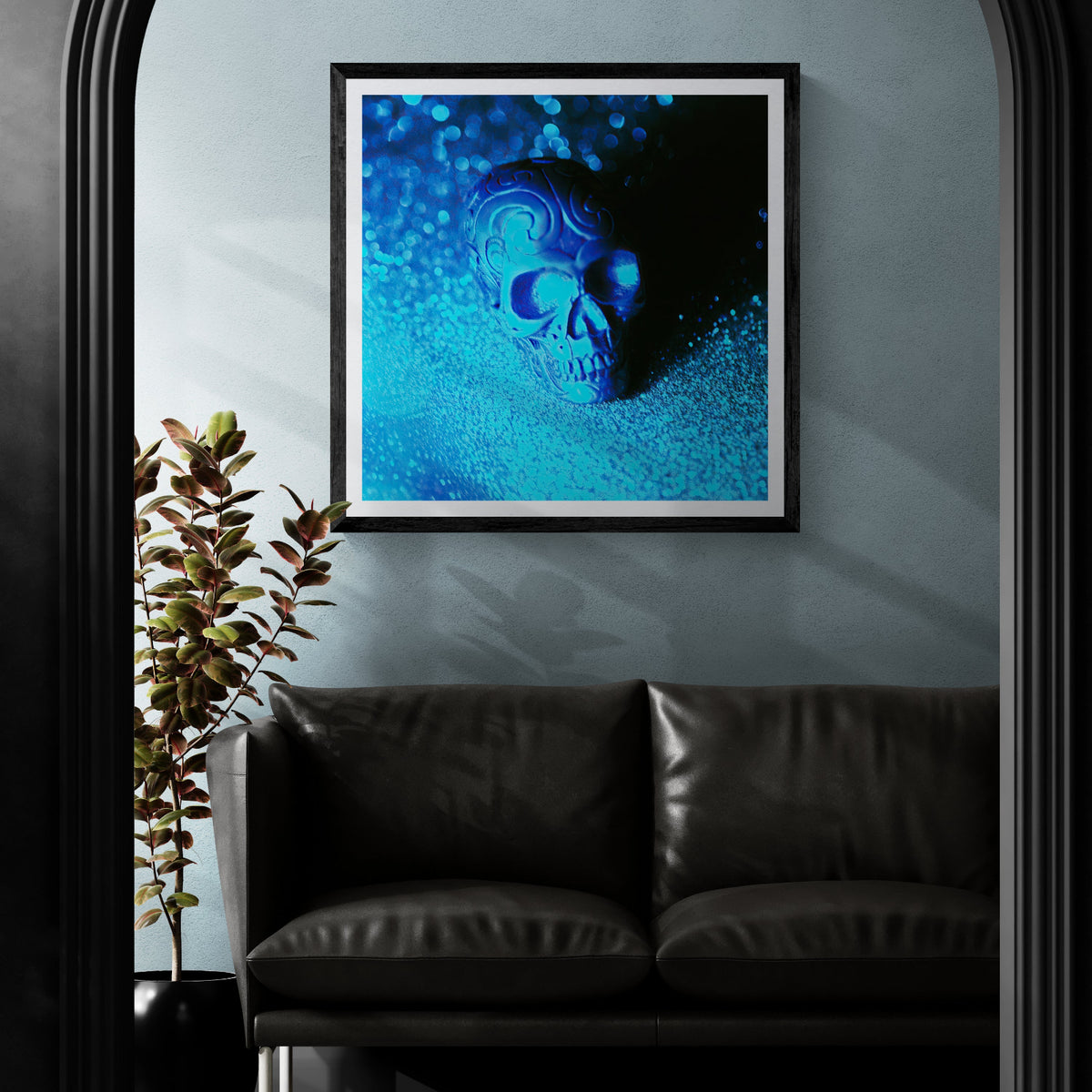 Glitter Remains blue-lit ornamental skull photography art print displayed as 30 × 30 wall art in a black frame above a black leather sofa.