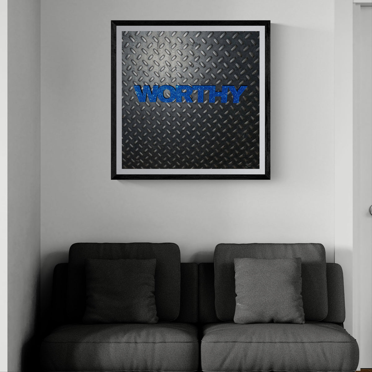 Worthy blue typographic art print on diamond plate displayed as 30 × 30 wall art in a black frame above a dark gray sofa.