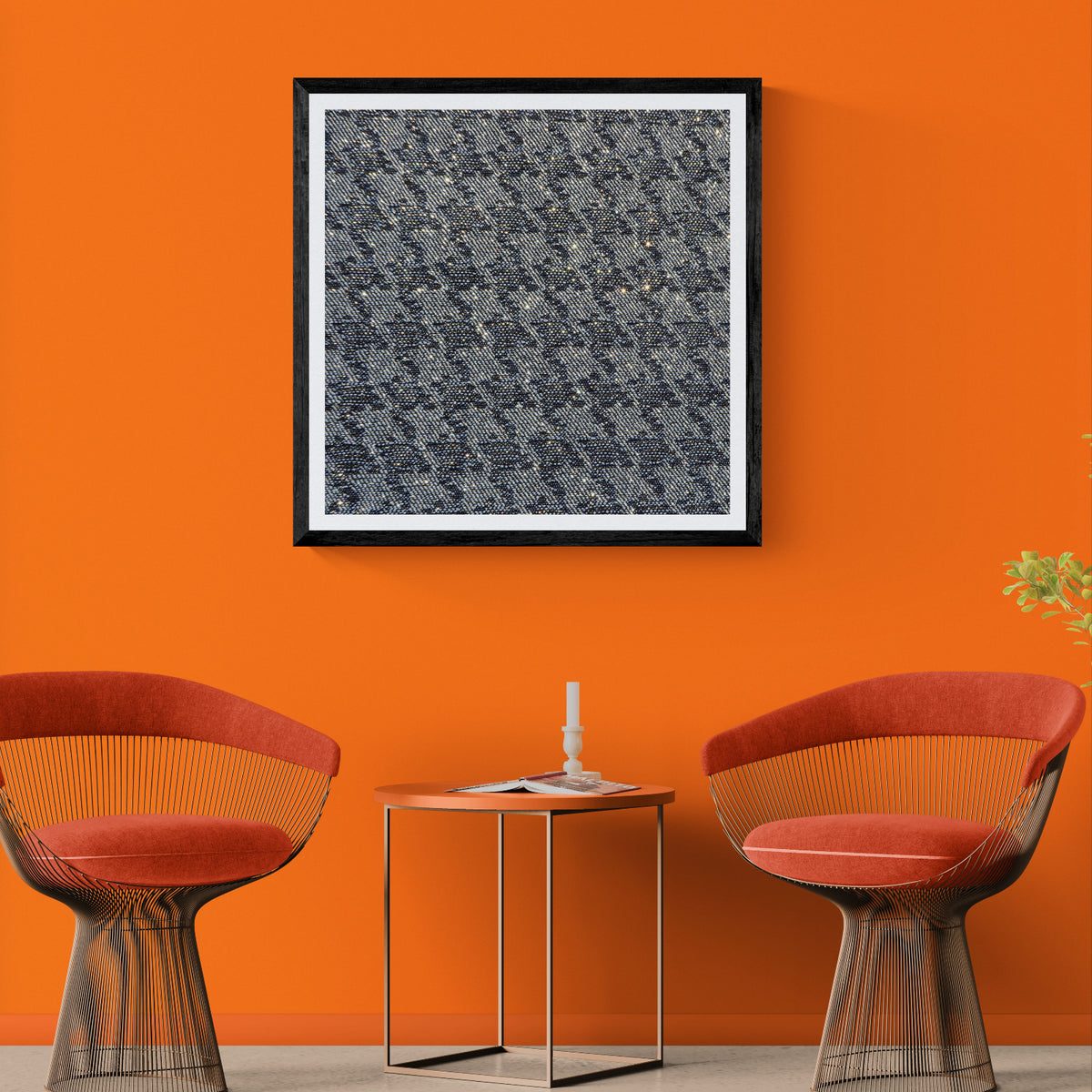 Woven Cosmos denim houndstooth photography art print displayed as 30 × 30 wall art in a black frame above two modern chairs on a vivid orange wall.